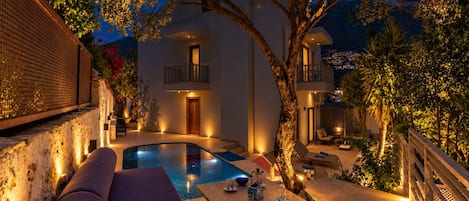 A poolside area with a lounge chair, a table with bowls, and a tree.
