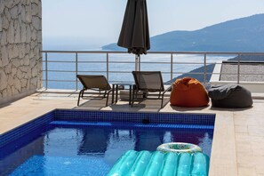 Un espace piscine sur le toit avec vue sur la mer, un petit matelas gonflable et des sièges.