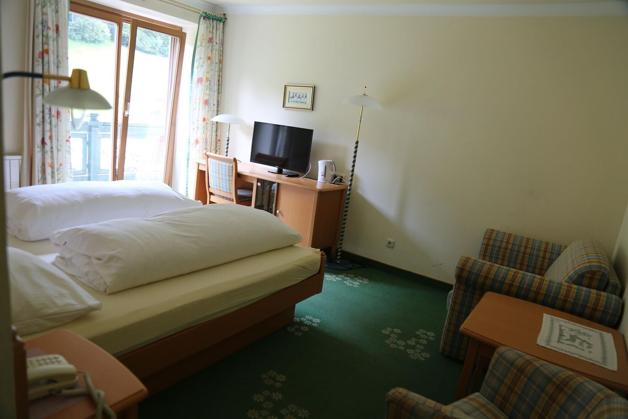 Quarto de hotel com cama, escrivaninha com televisão, uma cadeira e mesa pequena.