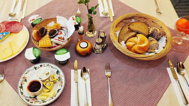 Una colazione con diversi cibi, utensili e una rosa su una tovaglia a quadri.
