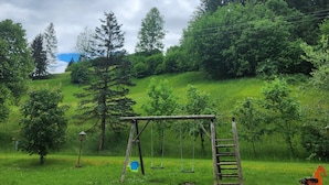 Un prato verde con altalene e scivolo in legno.