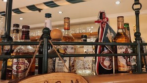 Un'area bar con diverse bottiglie di alcolici, un cartello in legno con su scritto 'Grill Goß' e uno schermo digitale.