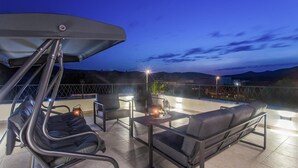Eine Dachterrasse mit zwei Sofas und einem Tisch, einem Baldachin und Blick auf die Stadt bei Einbruch der Dunkelheit.