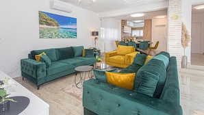 Ein modernes Wohnzimmer mit grünen Sofas, einem gelben Sessel und einem Essbereich mit Tisch und Stühlen.