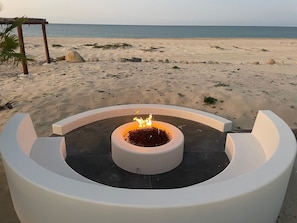 Una playa con un hogar circular en el centro rodeado de estructuras blancas.