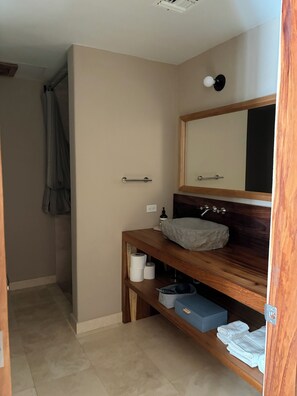Un baño con tocador de madera, lavabo, espejo, toallero y zona de ducha.