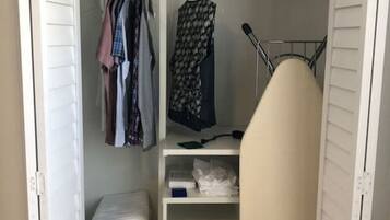 Un vestidor amplio con estantes, ropa colgada y una plancha.