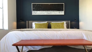 Ein Schlafzimmer mit Bett, einer Bank, einem Wandbild und einem Nachttisch.