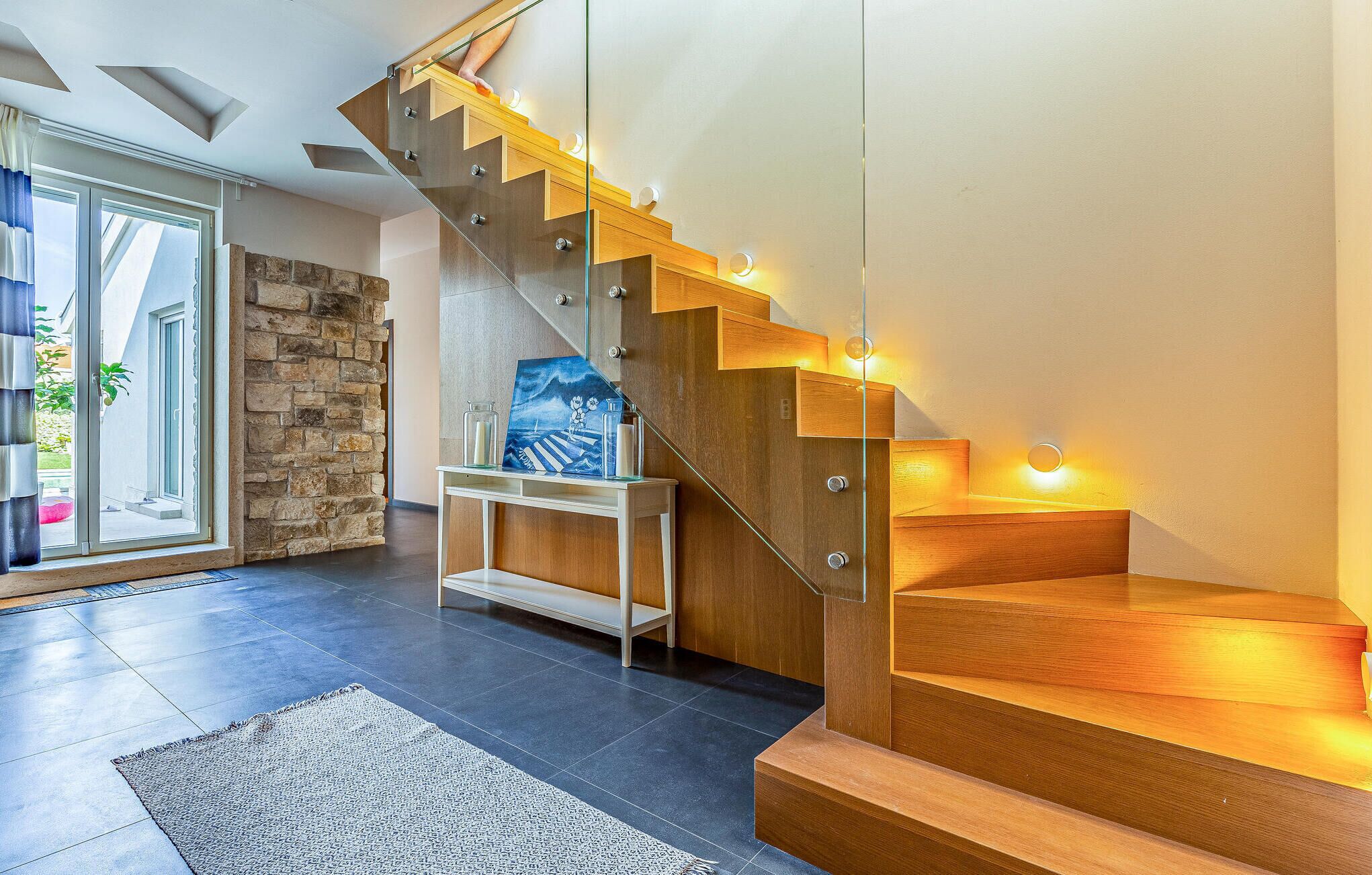 Una escalera moderna con barandillas de cristal y peldaños de madera que conduce a un segundo piso.