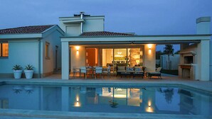 A modern house with a swimming pool, a patio with outdoor furniture, and a well-lit interior. - Awesome home in Banjole (Banjole)