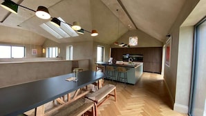 Eine geräumige Küche mit einer langen Arbeitsplatte, Holzböden und Pendelleuchten.