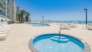 Un espace piscine comprenant plusieurs piscines, des chaises longues et un bâtiment doté de balcons.