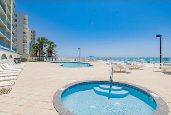 Un espace piscine comprenant plusieurs piscines, des chaises longues et un bâtiment doté de balcons.