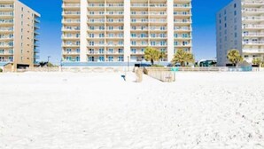 Un hôtel situé en bord de mer, avec plusieurs étages, des balcons et une plage de sable au premier plan.
