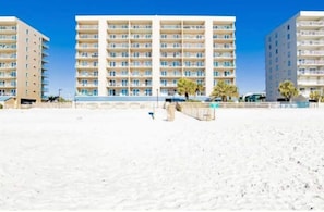 Un hôtel situé en bord de mer, avec plusieurs étages, des balcons et une plage de sable au premier plan.