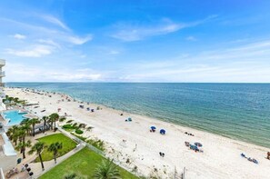 Une plage avec une piscine et des parasols, un ciel dégagé et une vue sur l’océan.