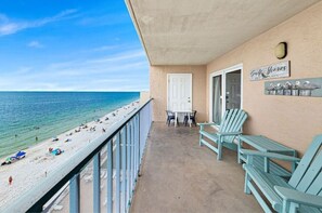 Un balcon avec vue sur la plage et l’océan, comprenant des fauteuils Adirondack, une table et une porte.