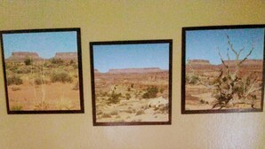 A bedroom with a brown sofa, a bed with a floral quilt, and three framed desert landscape pictures on the wall. - Rocking J Ranch House (Cove)