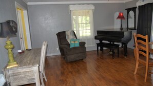 A living room with a piano, a chair with a dragonfly pillow, a lamp, and a mirror. - Rocking J Ranch House (Cove)