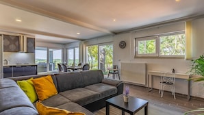 A modern living room with a grey sectional sofa, a dining area with a table and chairs, and a kitchen area with a stove and cabinets. - Luxurious home in Rovinj (Rovinj)