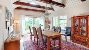 A dining room with a wooden table, six upholstered chairs, a chandelier, and a wooden cabinet with glass doors. - Awesome home in Genarp with WiFi (Genarp)