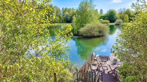 A wooden deck with chairs and a table overlooking a calm river, surrounded by lush greenery. - Awesome home in Genarp with WiFi (Genarp)