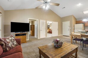 A spacious living room with a flat-screen TV, a ceiling fan, and a dining area with a table and chairs.