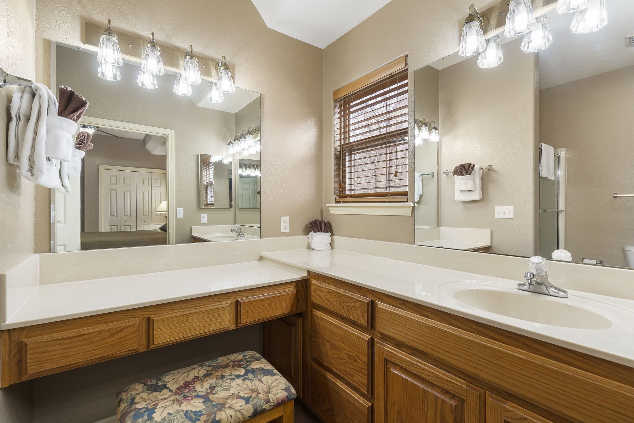 A bathroom with two sinks, wooden cabinetry, a bench, and multiple mirrors.