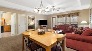 Un salón espacioso con zona de comedor, un sofá rojo, un ventilador de techo y un televisor.