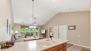 A kitchen with a large island, a dining area with a table and chairs, a ceiling fan, and a view of the outdoors.