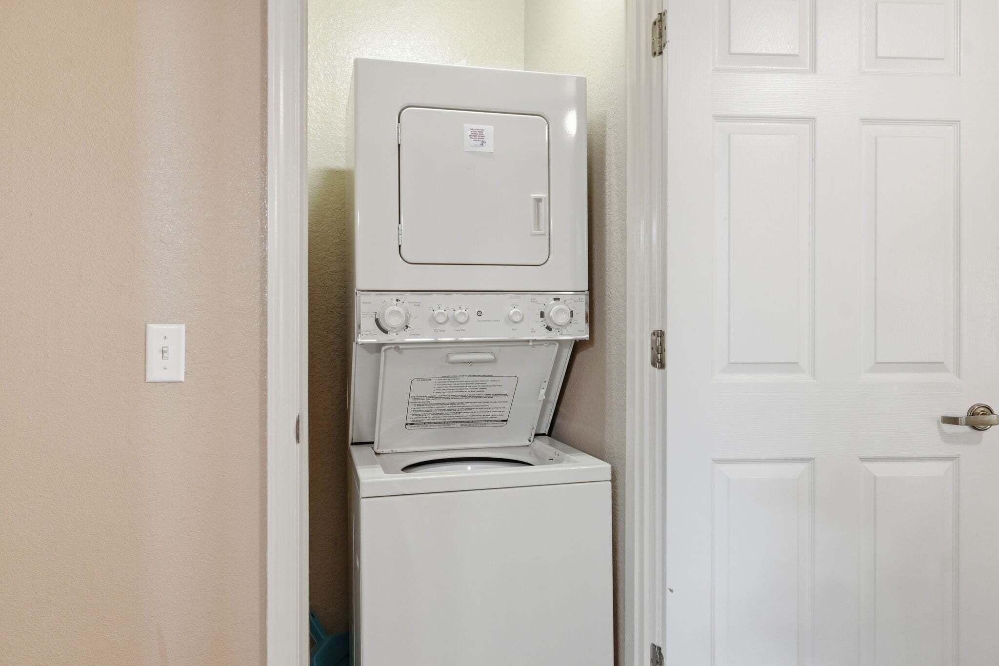 A stacked washer and dryer unit in a hallway with a white door on the right.