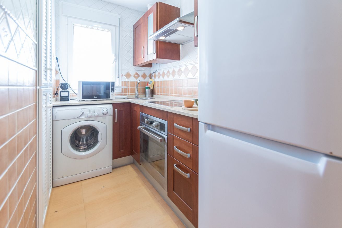 A compact kitchen with a washing machine, oven, and a refrigerator.