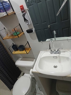 A bathroom with a white sink, toilet, and shelves with toiletries.