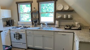 Una cocina moderna con armarios blancos, estufa a gas, lavavajillas y pileta. Hay dos ventanas que proveen luz natural, y un tapete negro en el piso.