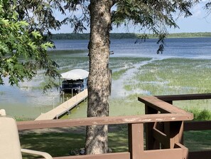 Um cais se estende por um lago, com um barco coberto por um toldo, cercado por árvores e áreas gramadas.