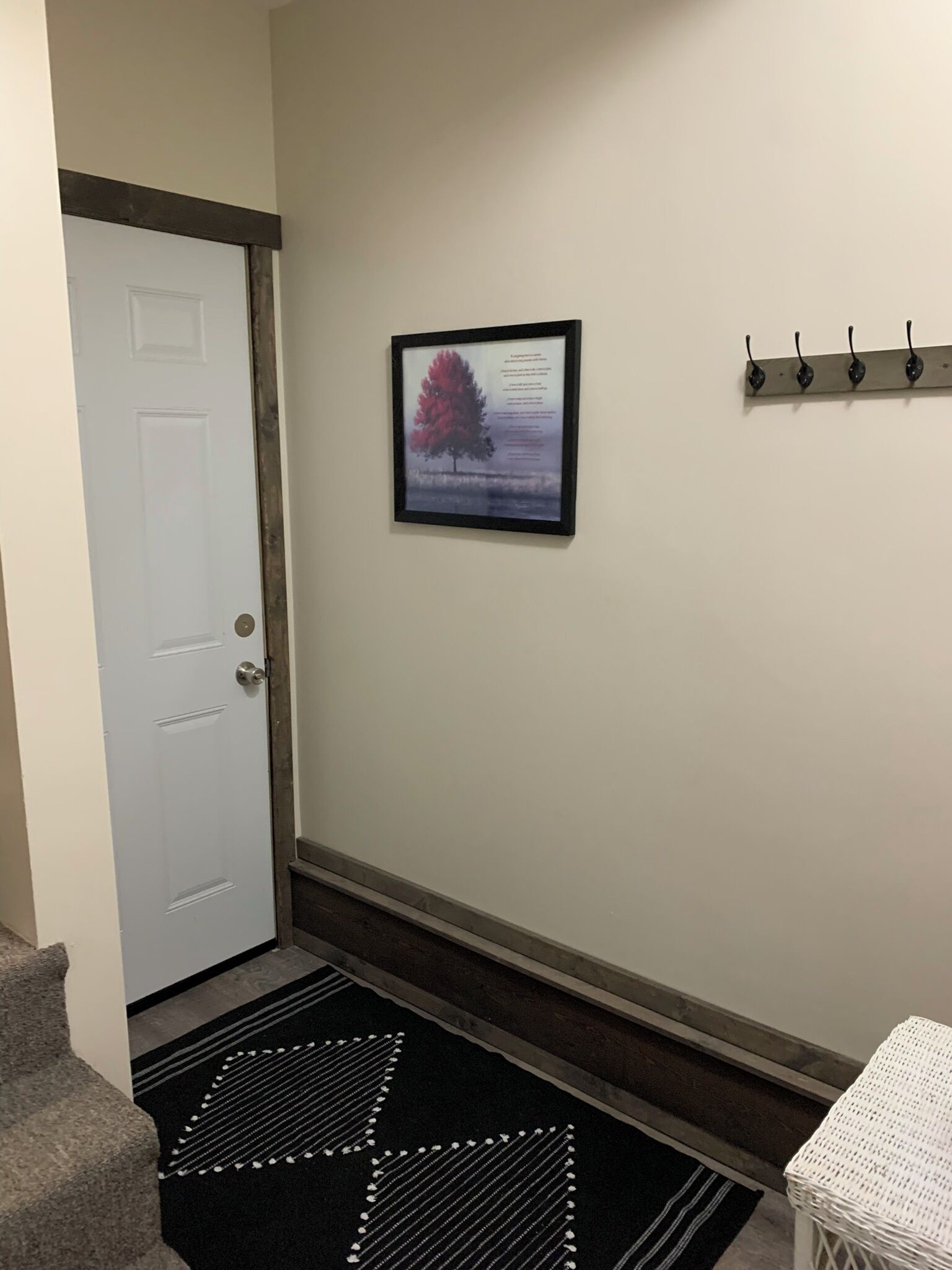 A hallway with a white door, a framed picture on the wall, a black and white rug, and a white basket.