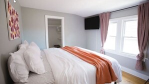 Un dormitorio con una cama, un televisor montado en la pared y un ventanal con cortinas.
