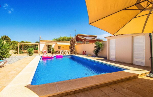 Una piscina con una sombrilla amarilla, una palmera y una casa al fondo.