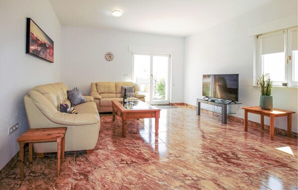 A living room with a beige sofa, a wooden coffee table, a TV on a stand, and a large window with a view of the outdoors. - Cozy home in Orihuela (Orihuela)