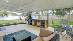 An outdoor patio with a glass-top table, wicker furniture, and a built-in barbecue grill. - Pet-Friendly Cocoa Beach Home: Walk to Beach! (Cocoa Beach)