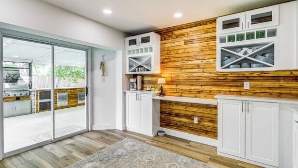 A modern kitchen with white cabinetry, a wooden accent wall, and a sliding glass door leading to a patio area. - Pet-Friendly Cocoa Beach Home: Walk to Beach! (Cocoa Beach)