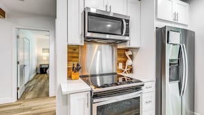 A modern kitchen with white cabinetry, a stainless steel microwave, a built-in oven, and a refrigerator. - Pet-Friendly Cocoa Beach Home: Walk to Beach! (Cocoa Beach)