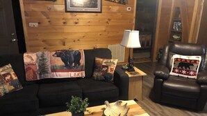 A cozy living room with a wooden wall, a black leather sofa, a wooden coffee table, and a leather armchair.