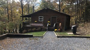 A rustic cabin with a gravel driveway, surrounded by autumn foliage.