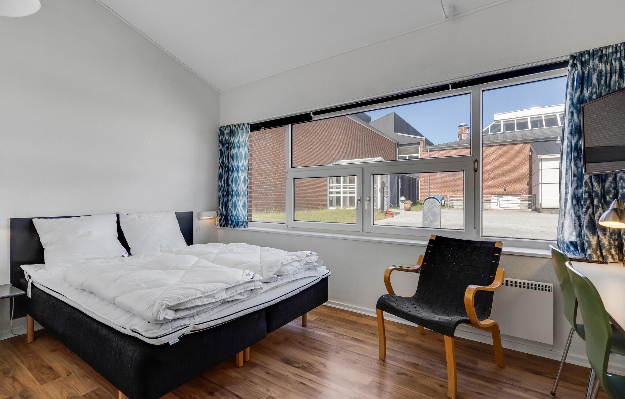A bedroom with a bed, a chair, and a window.