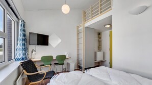 A modern hotel room with a bed, a desk, two chairs, a TV, and a window with curtains. - Fanø Bad, værelse 22 (Fanø)