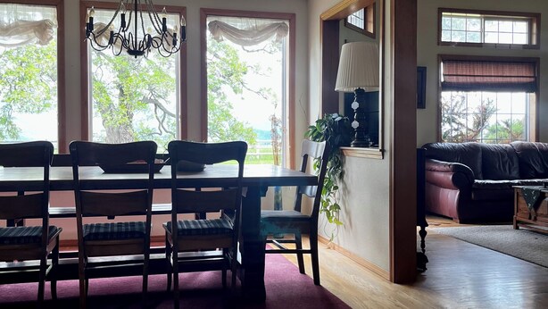 A dining area with a wooden table and chairs, a chandelier, and large windows with curtains. - Comfortable Montana Country Home for Family Getaways (Arlee)