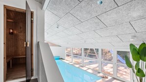Un intérieur moderne avec une grande baie vitrée donnant sur une piscine, une porte en bois et un plafond orné d’un motif géométrique original.