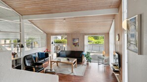 Un vaste salon doté d’un plafond en bois, d’un canapé en cuir noir, d’une table basse et d’un téléviseur fixé au mur.