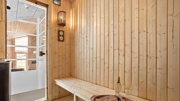 Un sauna en bois avec un banc, une horloge fixée au mur et une bouteille de vin posée sur le banc.